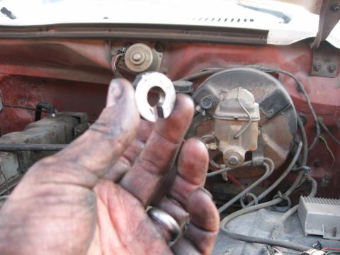 1981 Ford Bronco - Close-up of a hand holding a small metal component in front of the engine bay, showing the brake booster and master cylinder.