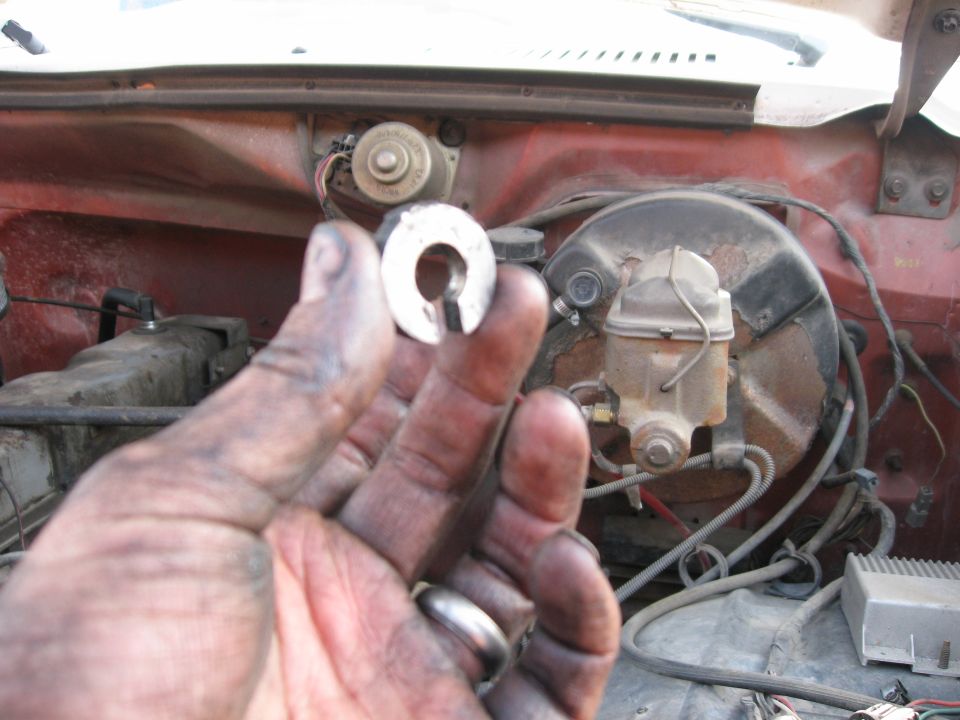 Hand holding metal part in engine bay with brake booster and master cylinder visible