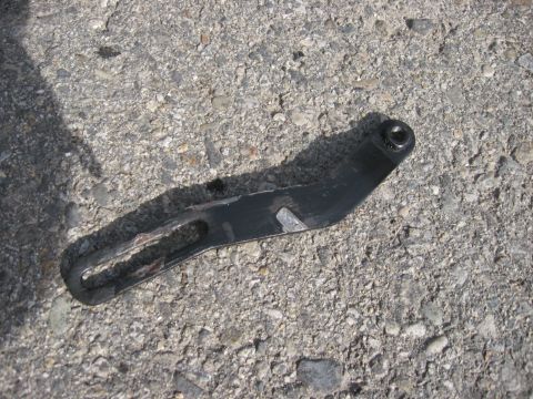 1981 Ford Bronco - A metal bracket is shown on a rough asphalt surface, with a shadow cast across it.