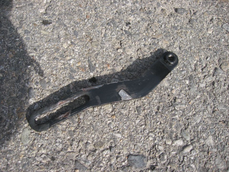 Black metal bracket with a slotted hole and a bolt hole, lying on asphalt