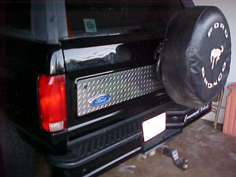 1995 Ford Bronco - Rear view of a black Ford Bronco, a diamond plate panel and a spare tire cover with the Ford Bronco logo.