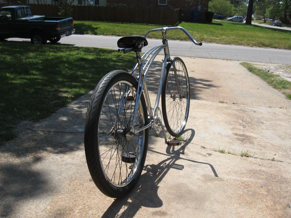 Chrome cruiser bicycle with wide tires parked on a concrete driveway. A dark pickup truck is visible in the background