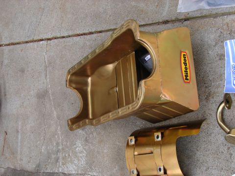 1973 Ford Ranchero - A gold-colored Milodon oil pan sits on a concrete surface next to other engine parts.