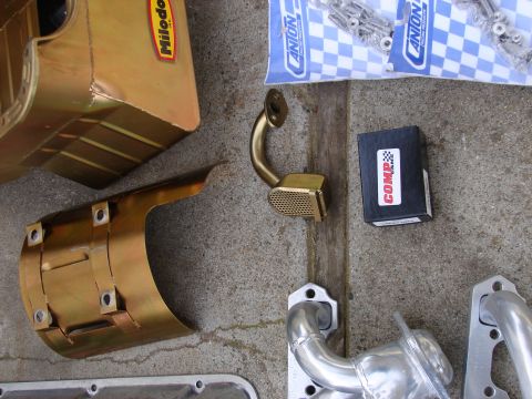1973 Ford Ranchero - Various engine performance parts including a Milodon oil pan, Comp Cams product, and Anion hardware are laid out on a concrete surface.