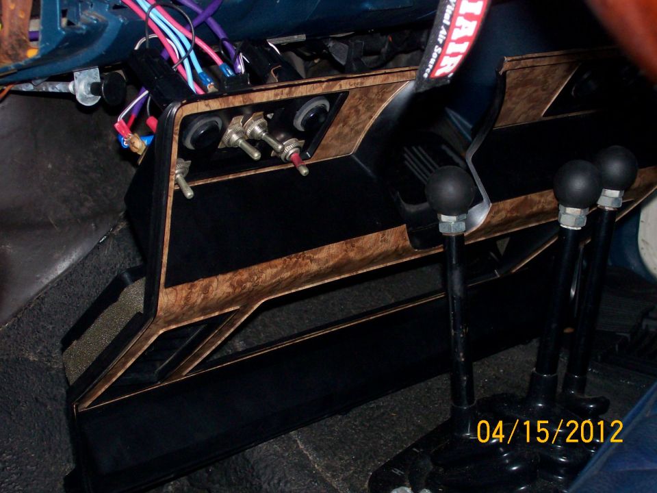 Interior shot of a vehicle's dashboard showing multiple toggle switches and three gear shifters, with exposed wiring