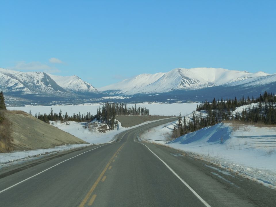 Winding asphalt road through a snowy mountain landscape under a clear blue sky