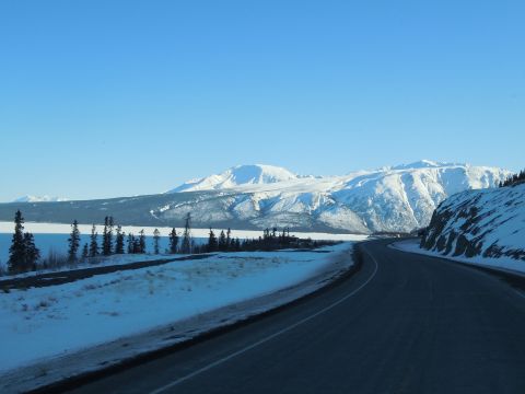 2009 Kenworth T800 - A clear blue sky overlooks a vast, snow-covered mountain range and a winding road.