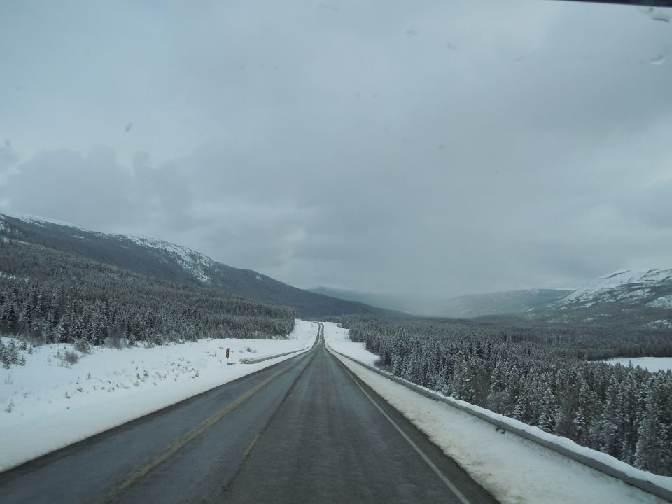 Highway through snowy forest and mountains under cloudy sky