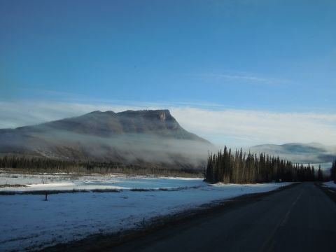 2009 Kenworth T800 - A road winds through a snowy landscape towards a misty mountain under a clear blue sky.
