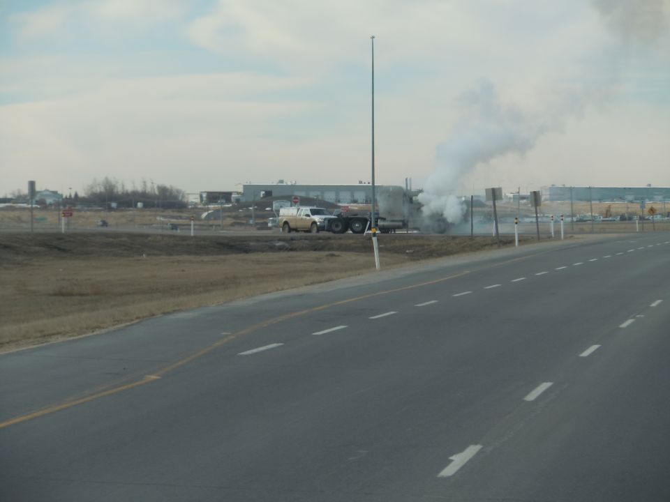 Side view of a truck emitting smoke on the side of a highway