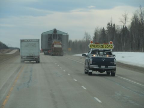 2009 Kenworth T800 - Oversize load escort truck leads two semi-trucks on a highway during daytime.