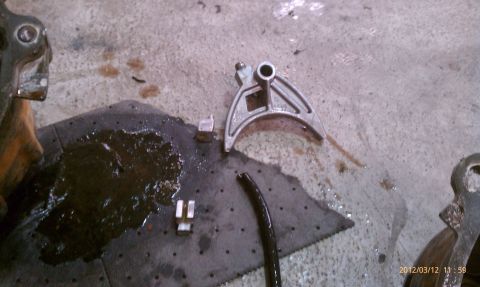 1987 Ford Bronco - Automotive part on a concrete floor with oil spill and other small metal pieces.
