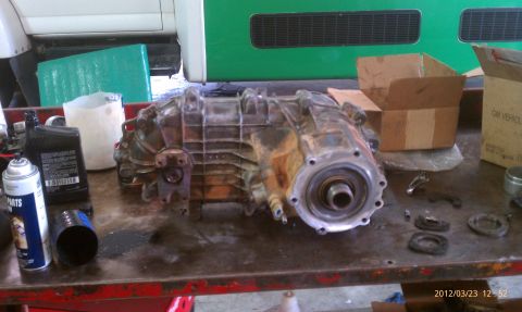 1987 Ford Bronco - A transmission part sits on a workbench next to automotive fluids and tools.