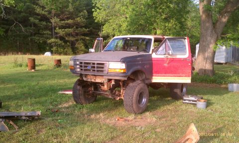 1987 Ford Bronco - A lifted Ford Bronco sits in a grassy yard with its doors open, showing a mismatched front end.