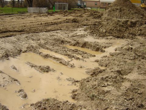 1984 Ford Mustang - A construction site is covered in mud and tire tracks, with several puddles of water.