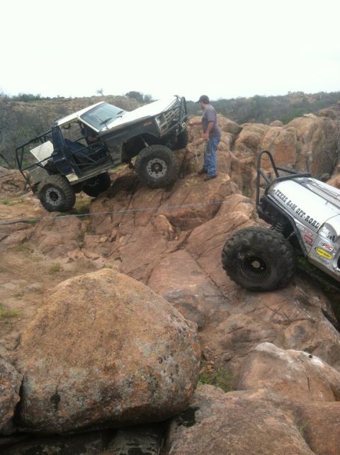 1986 Ford Bronco - Two modified off-road vehicles navigate a challenging rocky landscape.