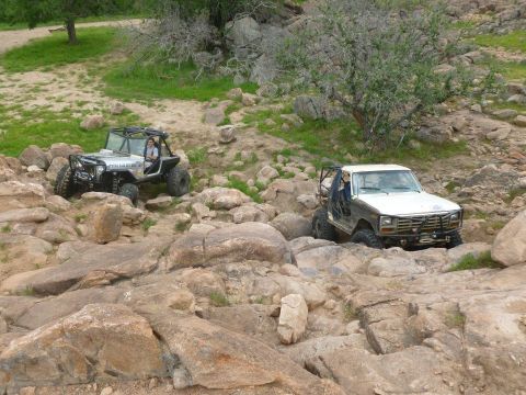 1986 Ford Bronco - A white 1980s Ford Bronco navigates a challenging rocky trail alongside another off-road vehicle.