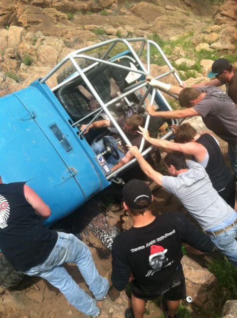 1986 Ford Bronco - Off-roaders attempt to right a tipped-over blue vehicle on a rocky trail.