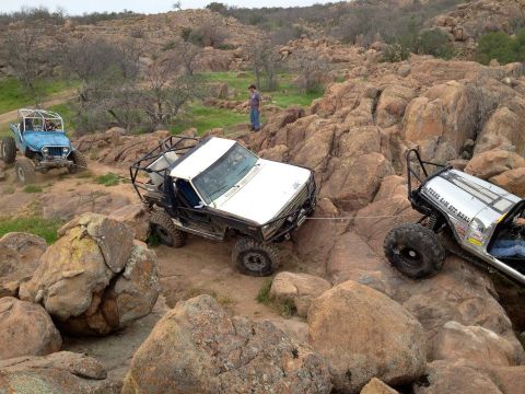 1986 Ford Bronco - Multiple off-road vehicles navigate a challenging rocky landscape, with one vehicle assisting another.