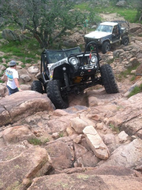 1986 Ford Bronco - Two off-road vehicles tackle challenging rocky terrain, with one jeep prominently featured navigating a difficult obstacle.