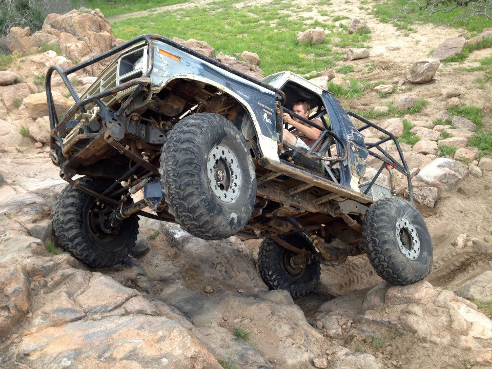 1986 Ford Bronco modified for off-roading, climbing over large rocks with a roll cage