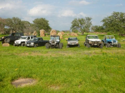 1986 Ford Bronco - A collection of off-road vehicles are gathered in a natural landscape under a cloudy sky.