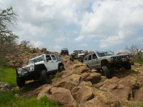 1986 Ford Bronco - Several off-road vehicles navigate a challenging rocky trail under a cloudy sky.