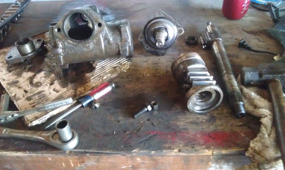 Disassembled steering gear box and related parts on a workbench with tools