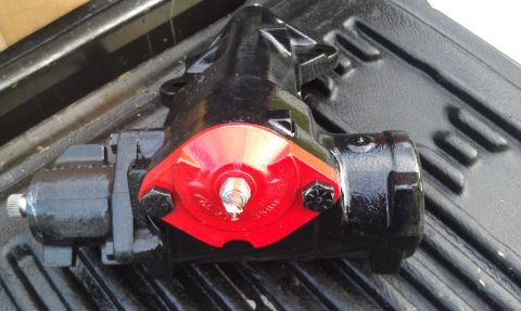 1978 Ford Bronco - Close-up of a black power steering gearbox with a red component, resting on a textured surface.