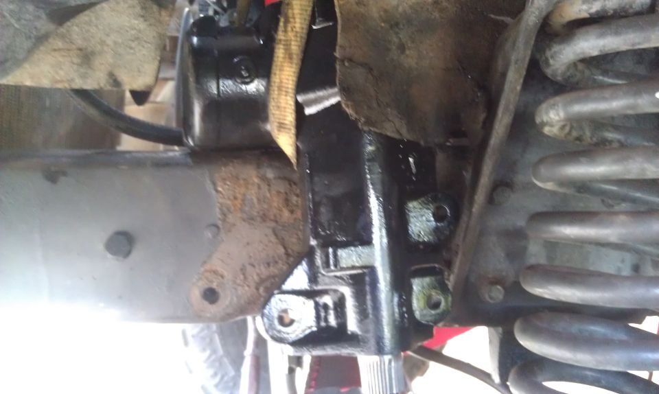 Close-up of a vehicle's steering gear assembly, showing the gearbox and part of a coil spring