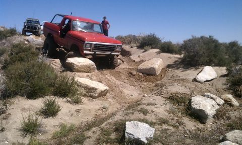 1978 Ford Bronco - A red SUV is shown off-roading on a rocky trail with another vehicle in the background.