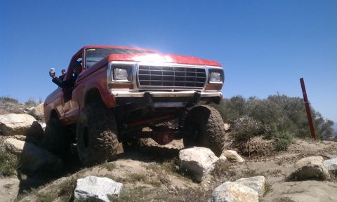 1978 Ford Bronco - A red 1978 Ford Bronco navigates a challenging rocky terrain under a clear blue sky.