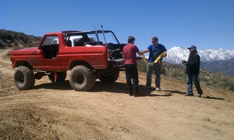 1978 Ford Bronco - A group of people stand around a red 1978 Ford Bronco on a dirt road, with snow-capped mountains in the background.