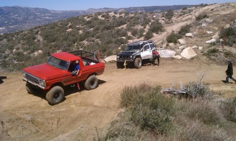 1978 Ford Bronco - Two off-road vehicles on a dusty trail in a hilly, arid landscape.