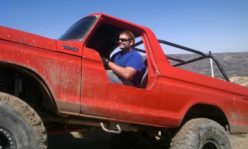 Guy in a red Bronco with a roll cage, covered in mud, driving off-road