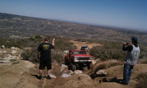 1978 Ford Bronco - Two off-road vehicles navigate a rocky trail with a vast landscape in the background.
