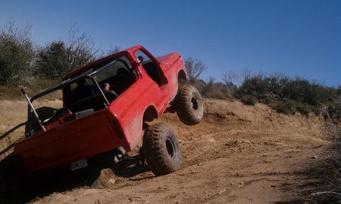 1978 Ford Bronco - A red 1978 Ford Bronco navigates a steep, dusty off-road trail under a clear blue sky.
