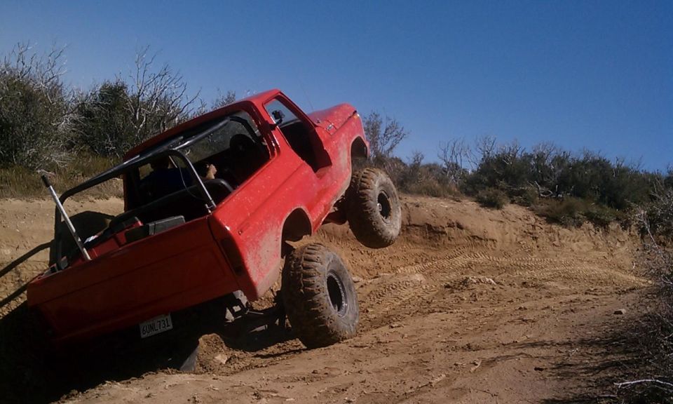 Red 1978 Ford Bronco with roll cage, lifted suspension, and large tires, climbing a dirt hill