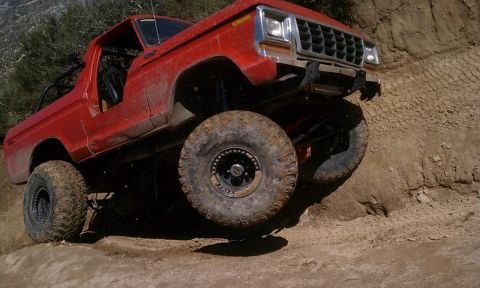 1978 Ford Bronco - This red 1978 Ford Bronco navigates a challenging off-road trail, its large tires gripping the dirt as it climbs.