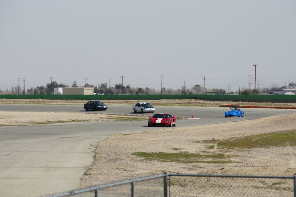 Race track with a red and white striped sports car, a blue open-wheel car, a white sedan, and a dark sedan