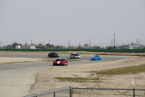 1995 Ford Taurus - A red sports car with white racing stripes navigates a turn on a race track, with three other vehicles visible.