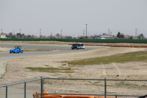 1995 Ford Taurus - A blue race car and two vans are seen on a track with a fence in the foreground.