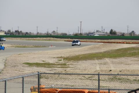 1995 Ford Taurus - White 1995 Ford Taurus navigates a turn on a race track, with a blue go-kart visible on the left.