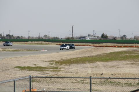 1995 Ford Taurus - Several cars are on a paved track with orange barriers and green fencing visible.