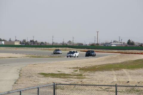1995 Ford Taurus - Three sedans navigate a turn on a race track under a hazy sky.