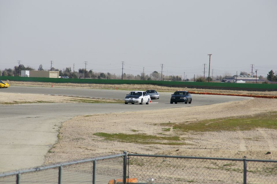 Three cars race on a track with a yellow car visible on the left