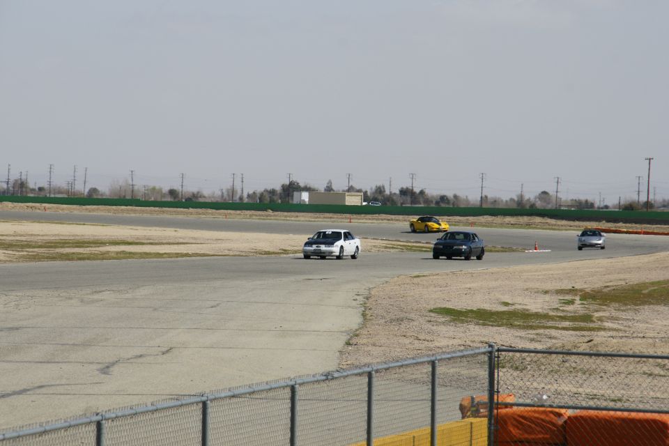 White car with black hood on race track, other cars visible