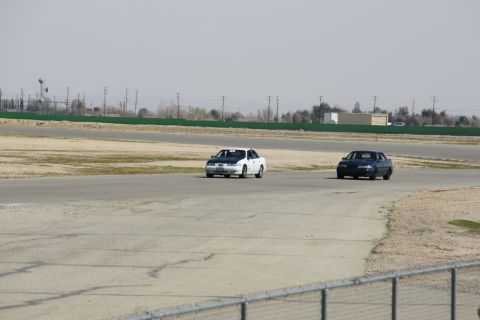 1995 Ford Taurus - Two sedans are seen on a racetrack under a hazy sky.