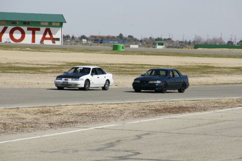 1995 Ford Taurus - Two sedans compete on a racetrack, with a building labeled 'TOYOTA' in the background.