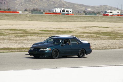 1995 Ford Taurus - A dark green 1995 Ford Taurus is seen on a race track, with another vehicle behind it.